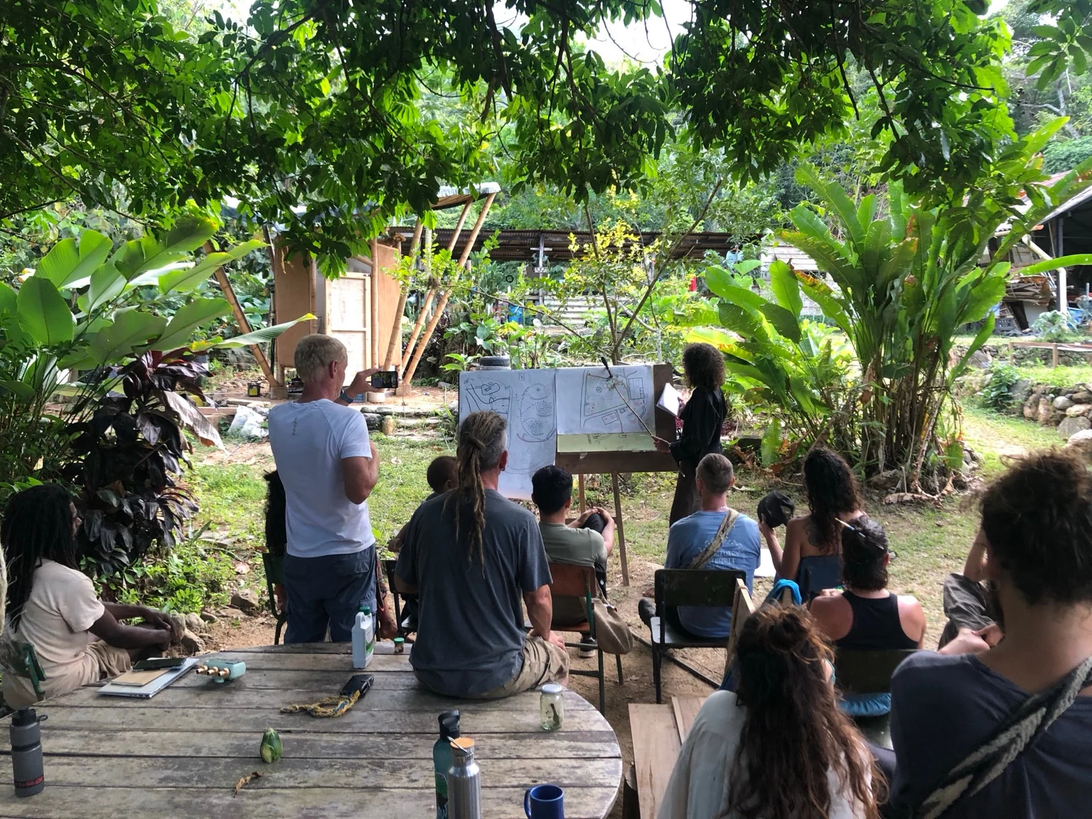 A group listening to an outdoor presentation of hand-drawn site designs.